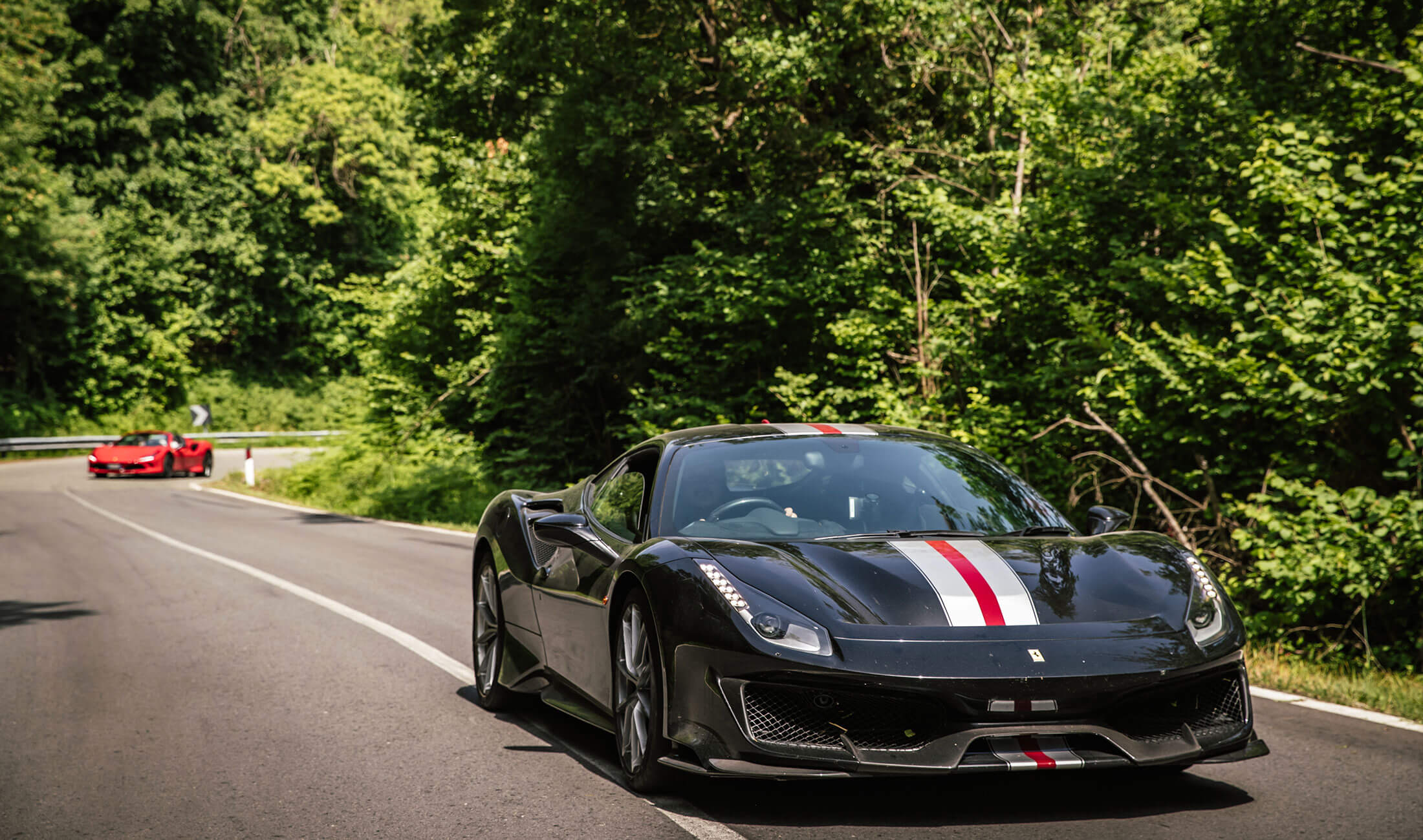 Black Ferrari with stripes in front of red Ferrari on country road in France