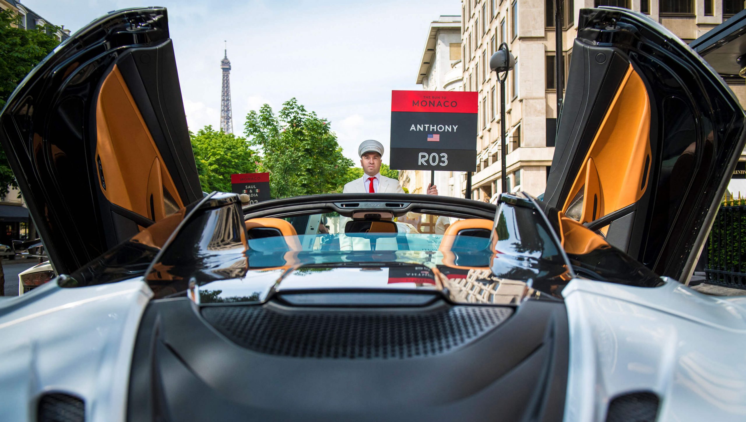 White Mclaren supercar with doors open in front of man holding sign and with Eiffel Tower in the background