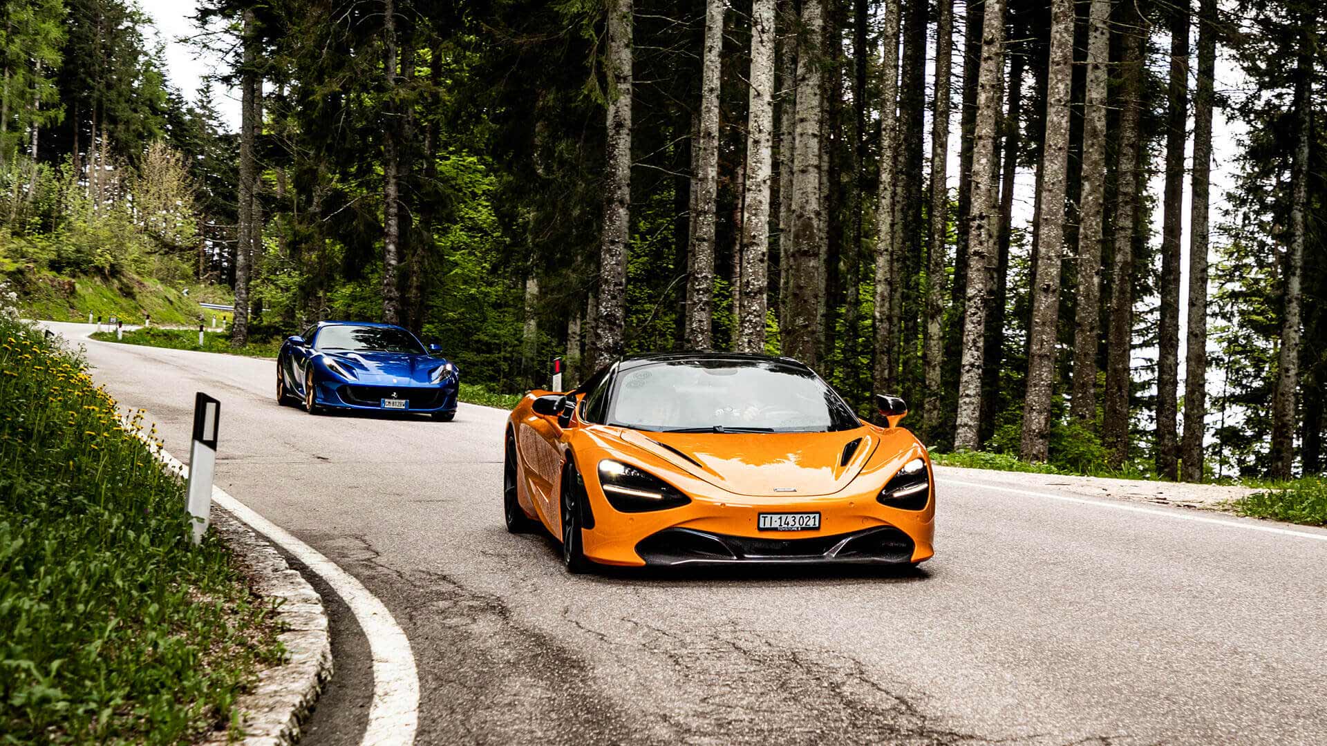 Supercars driving along a pine tree lined road in the Italian Alps